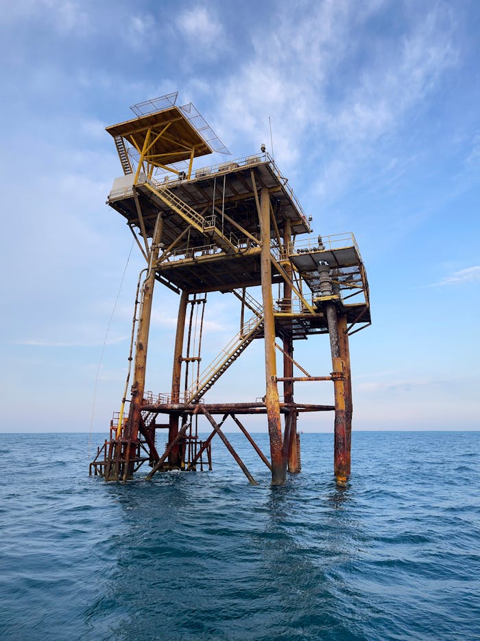 pexels-photo-13199842 Tall offshore oil platform structure in the middle of the ocean against a clear blue sky.
